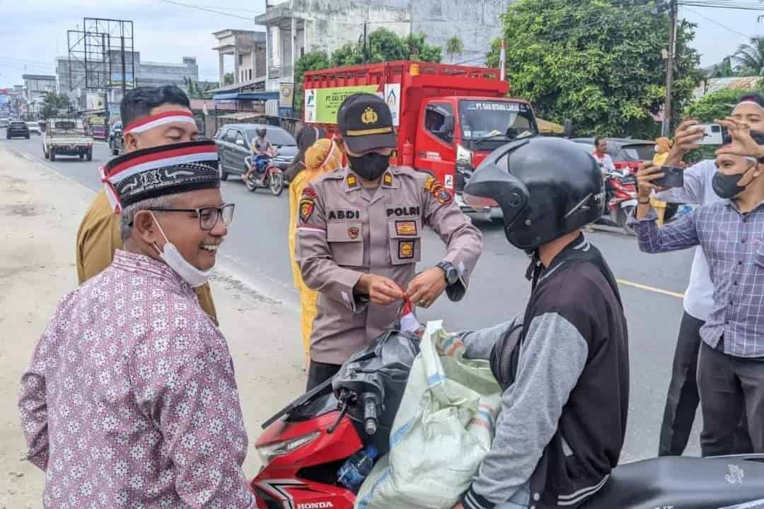 Plt Kapolsek Indrapura, Iptu Abdi Tansar didampingi Camat Air Putih, Rahmad Khaidir Lubis, dan tokoh masyarakat saat berbagi bendera merah putih. ( Foto: Sholeh Pelka).